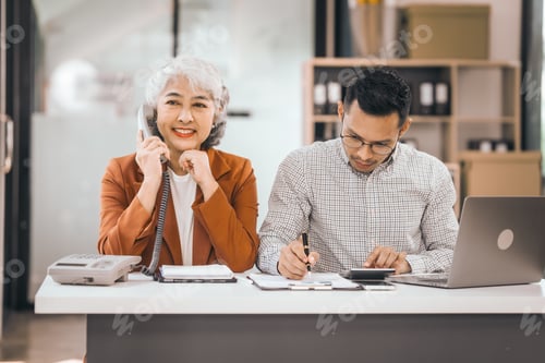 Preview: An older mature woman talks to asian man. They have a laptop and papers. The man looks stressed.