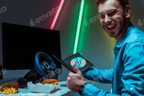 Preview: handsome and smiling man holding compact disk with video game and showing like