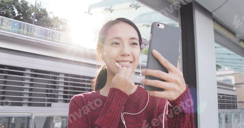 Preview: Woman talking video call on cellphone with earphone at outdoor