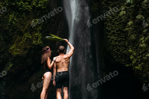 Preview: Beautiful couple at a waterfall in Indonesia, rear view. Man and woman at the waterfall