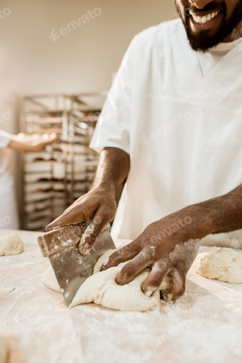 Preview: cropped shot of african american baker cutting dough with dough knife