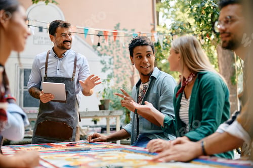 Preview: Multiracial group of happy friends talking to a waiter in a cafe.