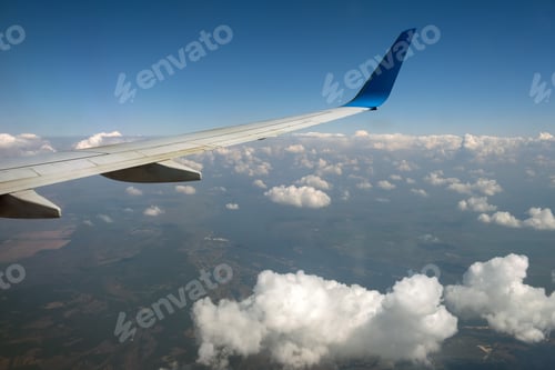 Preview: View of jet airplane wing from inside flying over white puffy clouds in blue sky. Travel and air