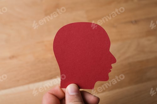 Preview: Closeup shot of a man holding a red icon of a man's head on a wooden background