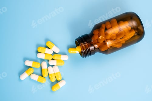 Preview: White and yellow pills scattered near opened bottle on blue background.