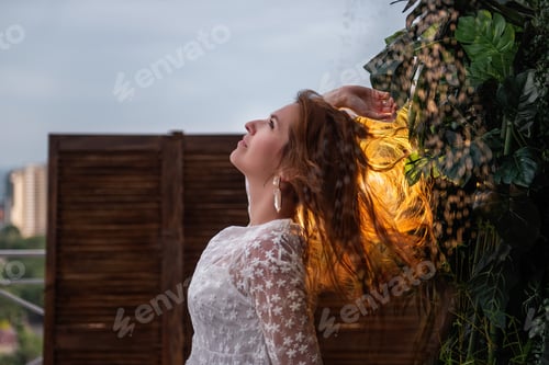 Preview: Young woman in white dress stands under the shower against wooden brown wall with tropical