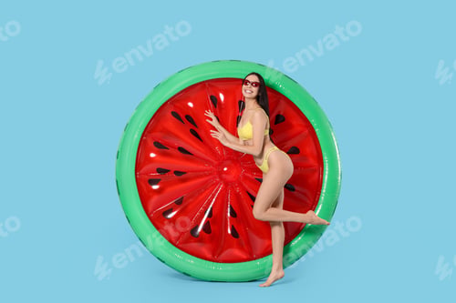 Preview: Young woman in stylish swimsuit near inflatable mattress against light blue background