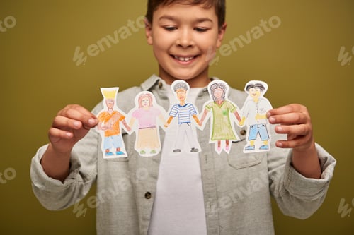Preview: Blurred and positive multiracial boy holding drawn paper characters during international child