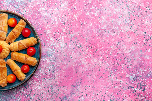 Preview: top view sweet delicious bagels baked pastries inside tray with plums on light-pink desk bake pastry