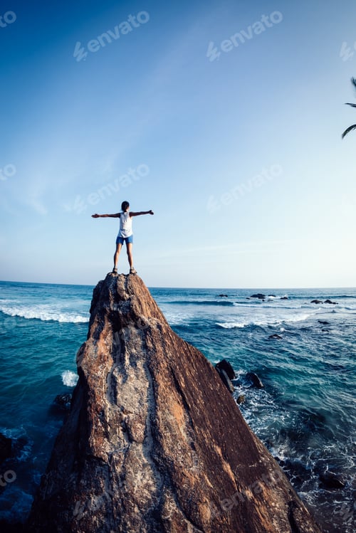 Preview: Successful woman outstretched arms on seaside rock cliff edge