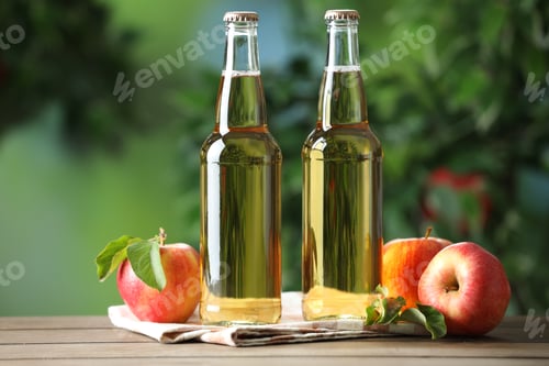 Preview: Delicious cider in glass bottles and apples on wooden table outdoors