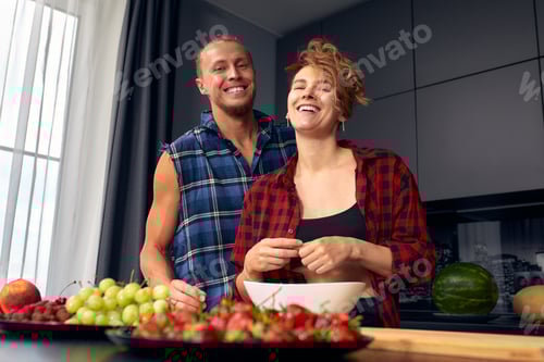 Preview: Happy couple standing in kitchen at home preparing together yummy dinner on first dating, spouses