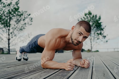 Preview: Motivational bearded man stands in plank pose, trains muscles and has strong body