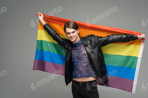 Preview: cheerful bigender person in black leather jacket posing with lgbt flag isolated on grey