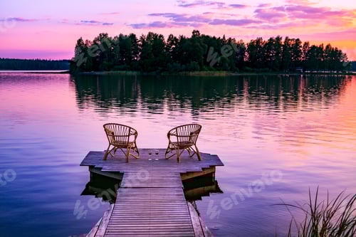 Preview: Two rattan chairs and glasses of red wine on a pier overlooking a lake at sunset in Finland