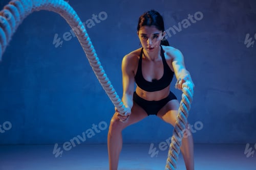 Preview: Caucasian young female athlete practicing on blue studio background in neon light