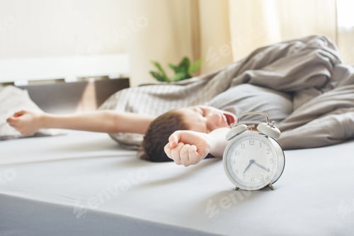 Preview: boy lying on the bed near alarm clock in the morning, stretching and yawns