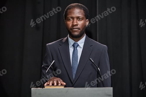 Preview: Male Politician with Hand on Constitution Taking Oath to Uphold Law Standing at Pulpit Indoors