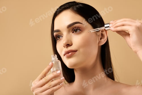 Preview: Young woman applying serum for glowing healthy skin in studio environment