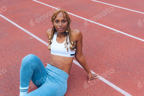 Preview: young sporty woman sitting on the running track exhausted