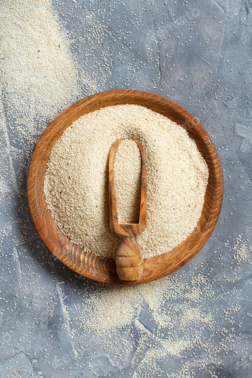 Preview: Raw uncooked fonio seeds with a spoon on a plate on grey background