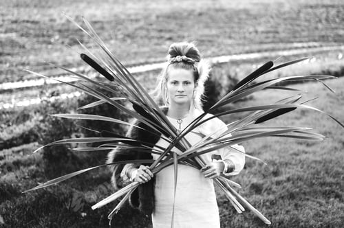 Preview: Strong young woman with a bulrush grass reed on rural field, portrait monochrome