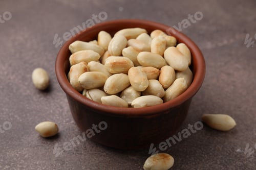 Preview: Roasted peanuts in bowl on brown table, closeup