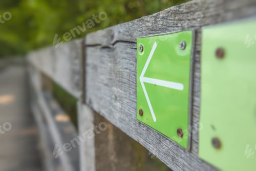 Preview: Selective focus shot of a green arrow sign on the wooden fence in a park
