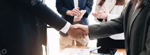 Preview: Two business men shaking hands while their colleagues applauding in the background