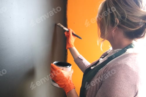 Preview: Woman painting black and orange wall wearing orange gloves