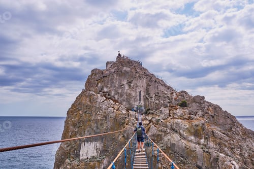 Preview: Man with backpack walks over suspension bridge to Diva Rock, Black Sea coast, near Yalta, Crimea.