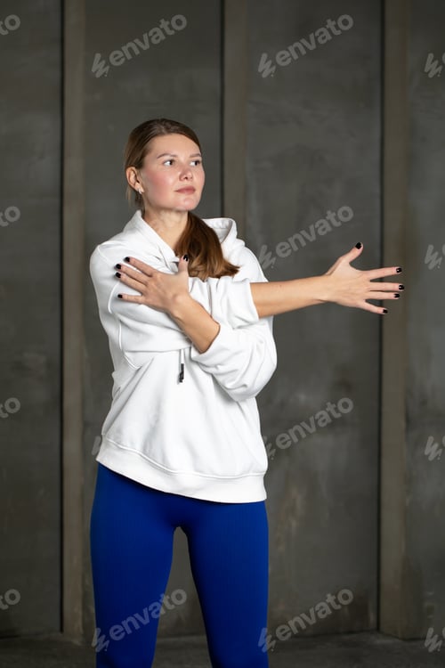 Preview: An athlete in leggings and a hoodie stretches her arm, warming up the shoulder muscles. Stretching