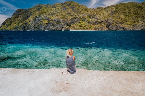 Preview: Tourist female rear view sitting pier edge on Matinloc island on hoping tour C. El Nido, Palawan