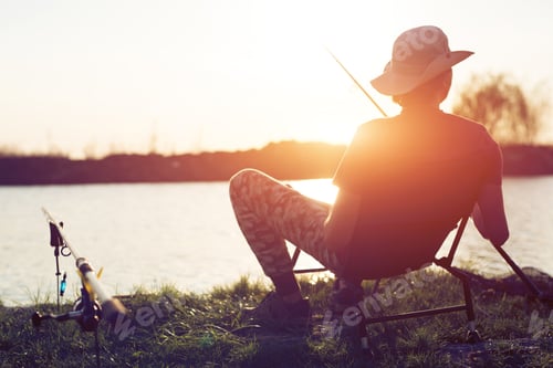Preview: Young man fishing on lake at sunset enjoying hobby