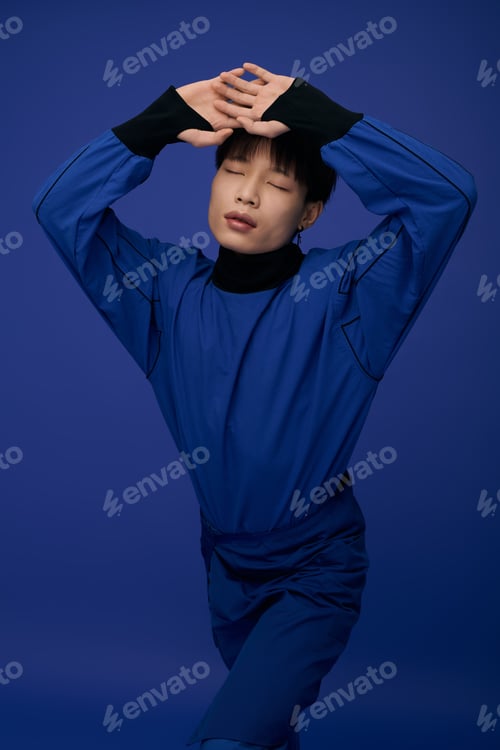 Preview: Young handsome asian man poses creatively against a vibrant blue background in stylish attire