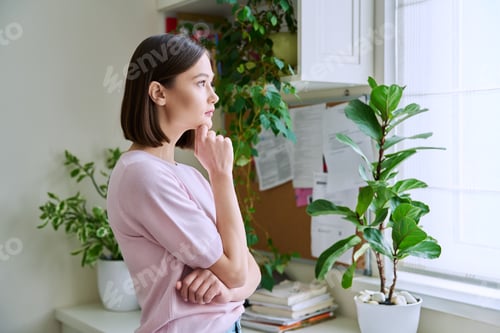 Preview: Serious young woman looking out the window, in home interior
