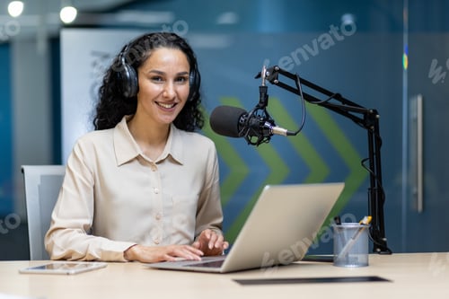 Preview: Smiling woman recording podcast with laptop and microphone in modern office
