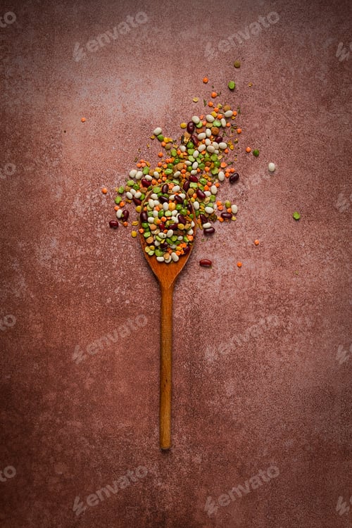 Preview: wooden spoon, with an assortment of legumes, beans, peas, top view, on a brown background,