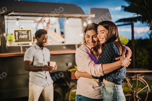 Preview: Cheerful girlfriends hugging near food truck