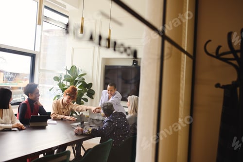 Preview: View through window of multiethnic businesswomen fist bumping and smiling in meting room