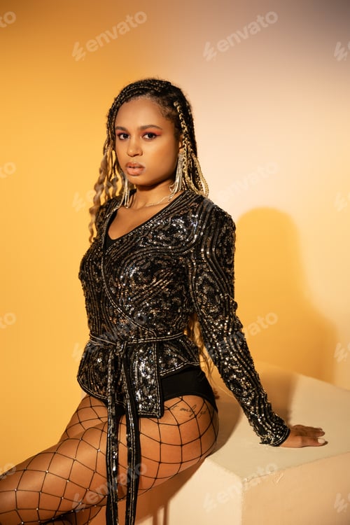 Preview: tattooed and beautiful woman with dark skinned posing in fishnet tights on yellow background, style