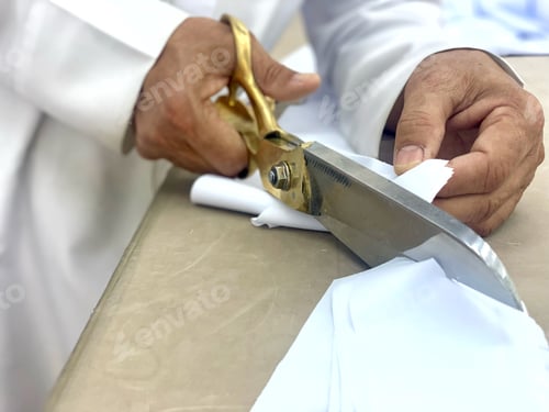 Preview: Middle East diverse dark skinned tailor wears traditional clothes as he cuts textile fabric