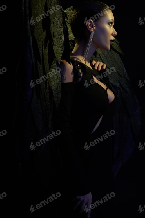 Preview: demonic charm, side view of sexy woman in halloween costume of dark demon with wings on black