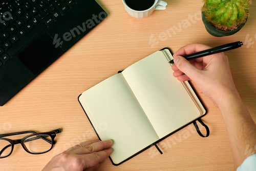 Preview: Man writes on a notebook on a wooden desk. Office, work from home