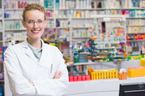Preview: Female pharmacist wearing coat using dispensing trays and monitor at pharmacy counter, copy space