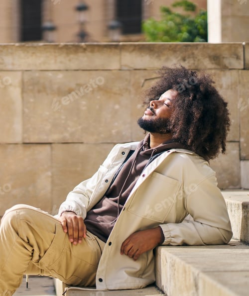 Preview: Portrait of a man with afro hair sitting on a step in the square