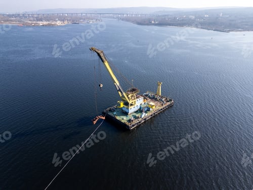 Preview: A floating crane barge with a large yellow crane operates on calm waters, lifting an object with its