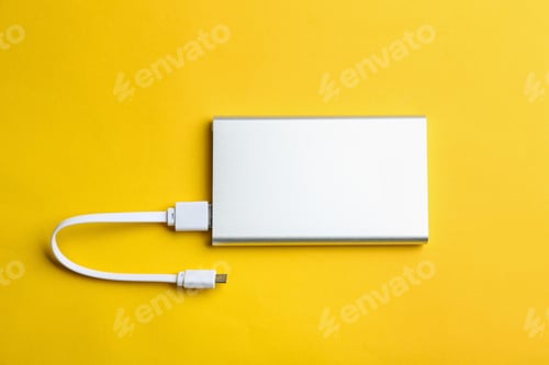Preview: Modern portable charger with cable on yellow background, top view
