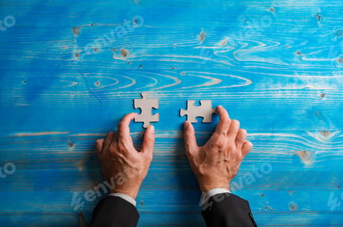 Preview: Top view of hands of a businessman holding two blank matching puzzle pieces