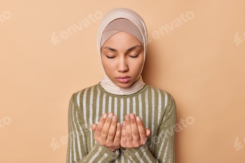Preview: Religious Muslim woman keeps eyes closed gestures stands in praying pose wears traditional hijab and